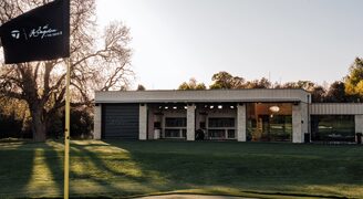 the rear elevation of the golf studio at the grove pictured at dusk with the taylormade flag visible in the foreground